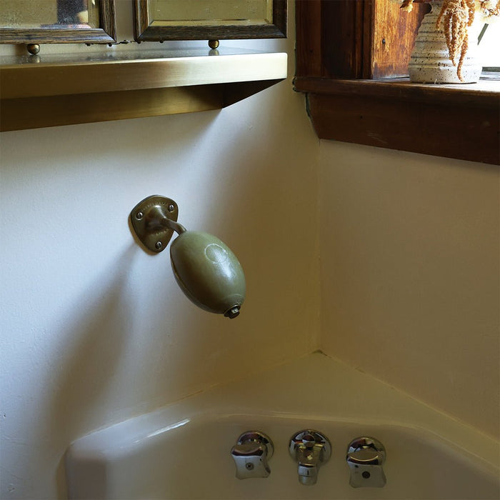 A brass wall-mounted soap holder with a rounded, olive-green bar of soap installed on a cream-colored wall above a sink.